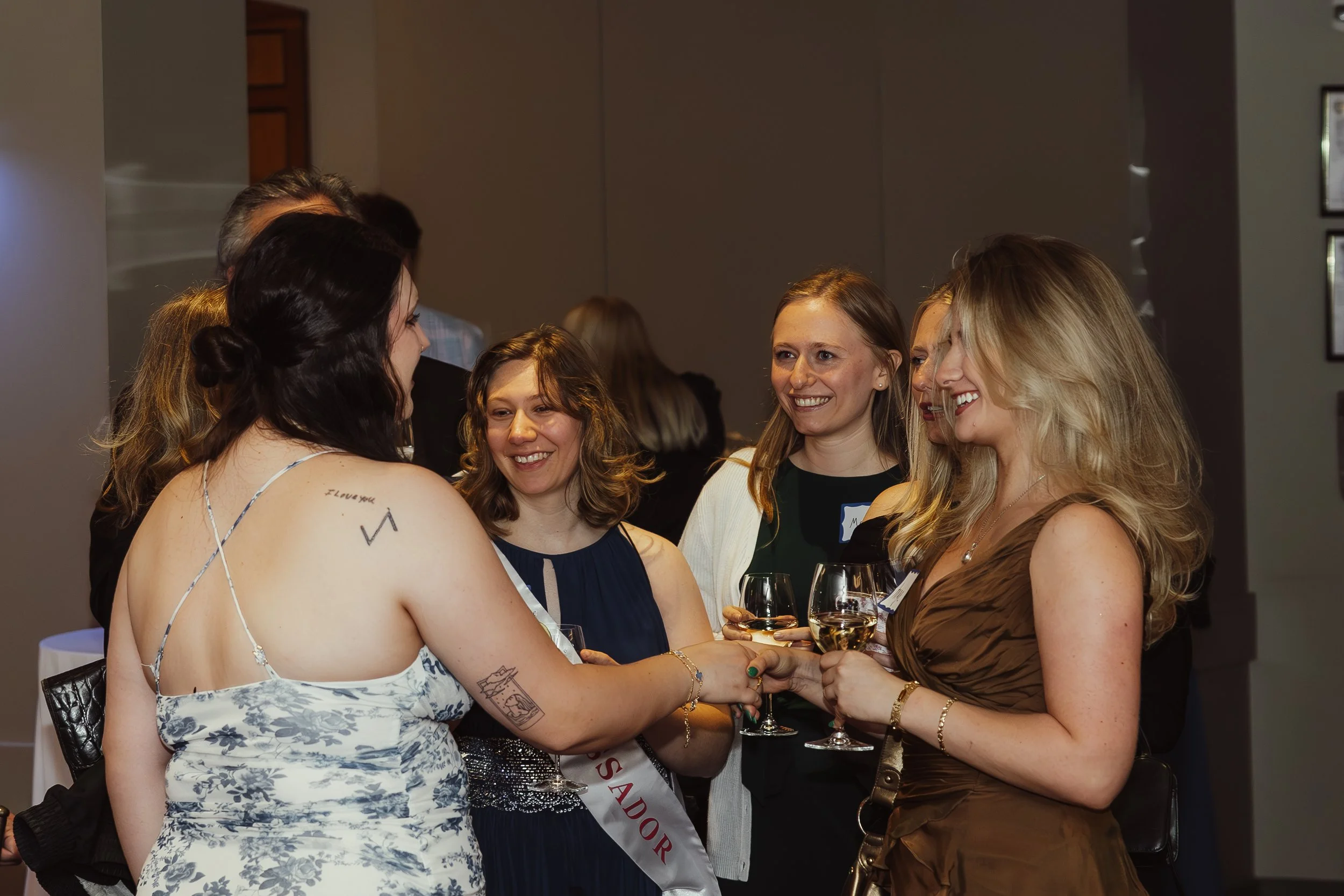 A group of women at a social gathering, smiling and talking while holding wine glasses.