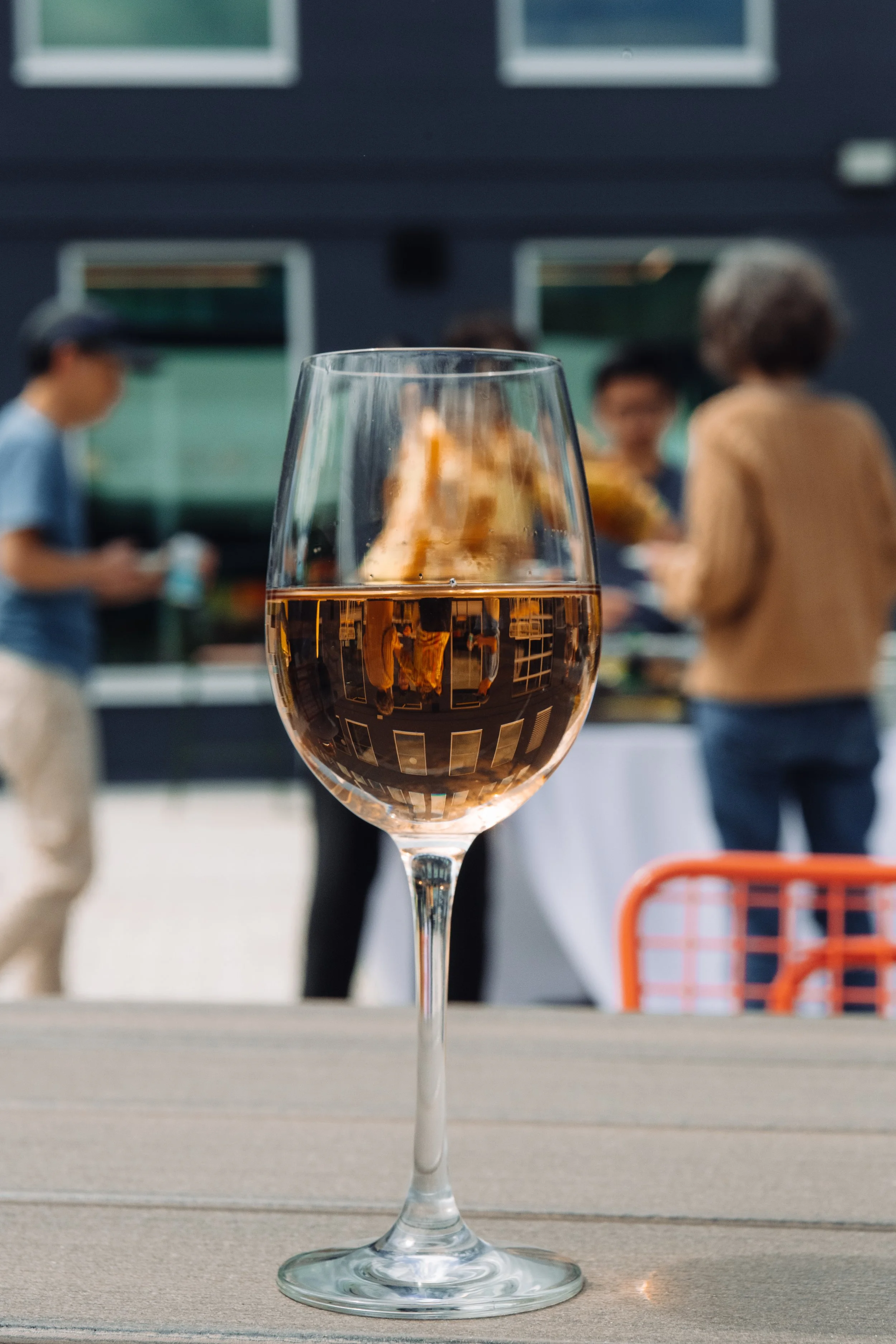 A glass of rosé wine on a wooden table with a background of people gathered outdoors.
