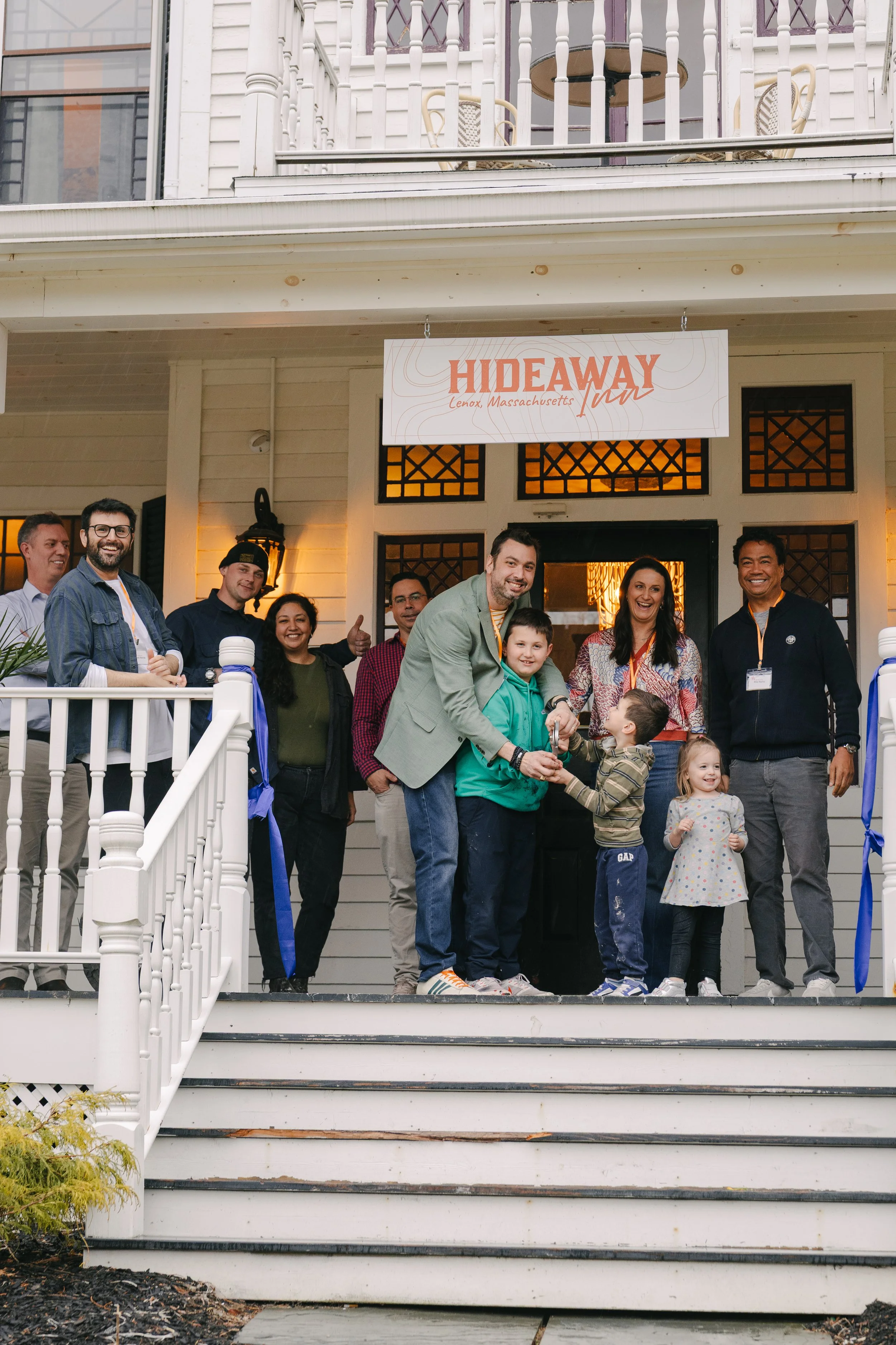 A group of people standing on the porch of a house, celebrating at an event with a sign that reads "HIDEAWAY" in Lenox, Massachusetts.
