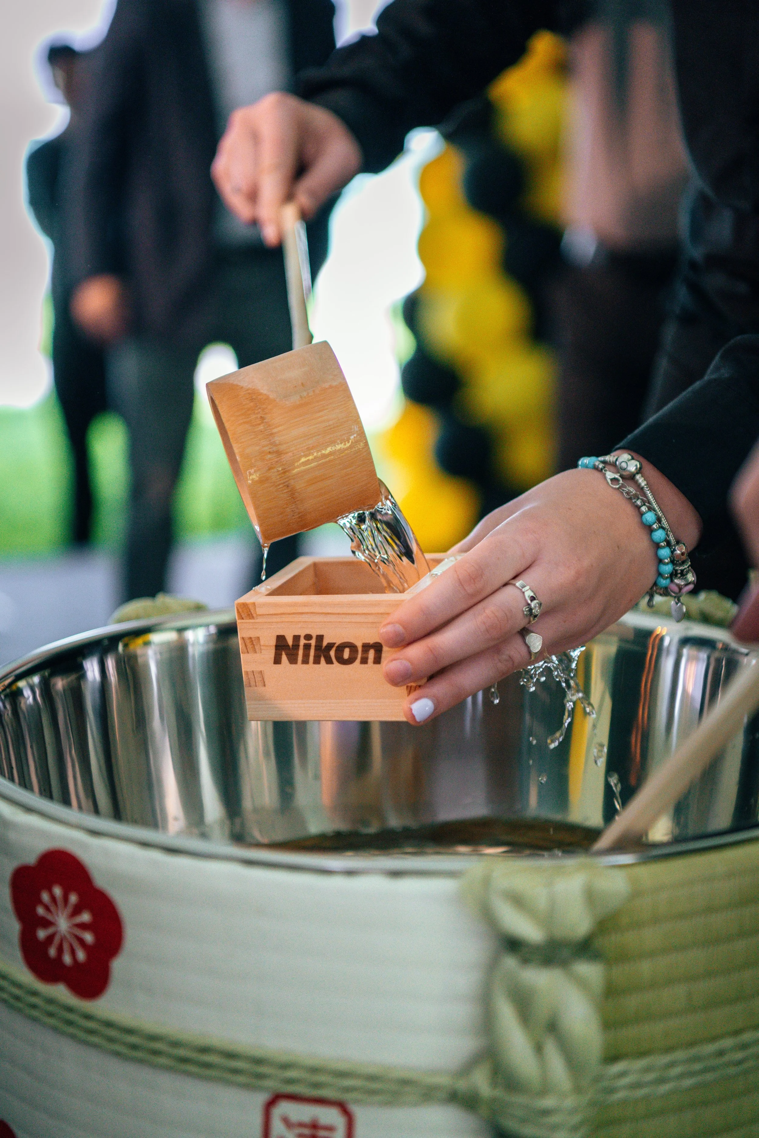 Person pouring water from a wooden scoop into a Nikken-branded container during a ceremony or event.