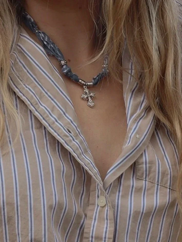 Close-up of a person wearing a striped button-up shirt and a dark beaded necklace with a cross pendant.