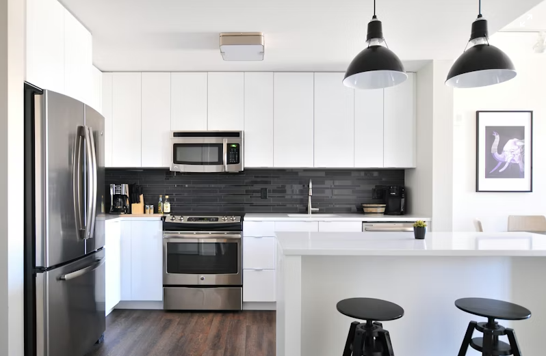 Modern kitchen with white cabinets, stainless steel appliances, black backsplash, and black hanging pendant lights