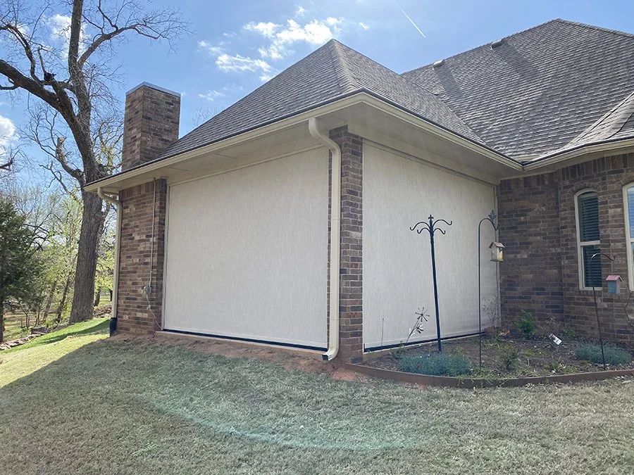 Rear view of a house with a closed white garage door, brick chimney, and a small garden area with a garden trellis and bird feeder.