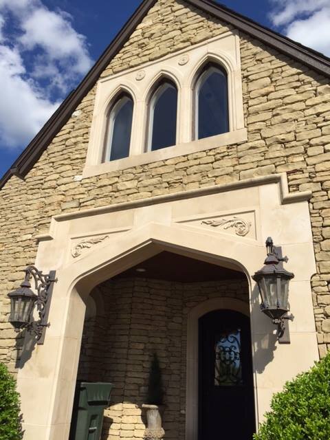 Close-up of a stone house facade with Gothic-style arched windows, decorative stonework, and two wall-mounted lanterns beside the doorway.