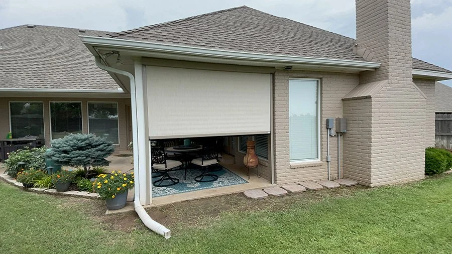 Back patio of a house with an open retractable awning, outdoor furniture, potted plants, and a chimney.