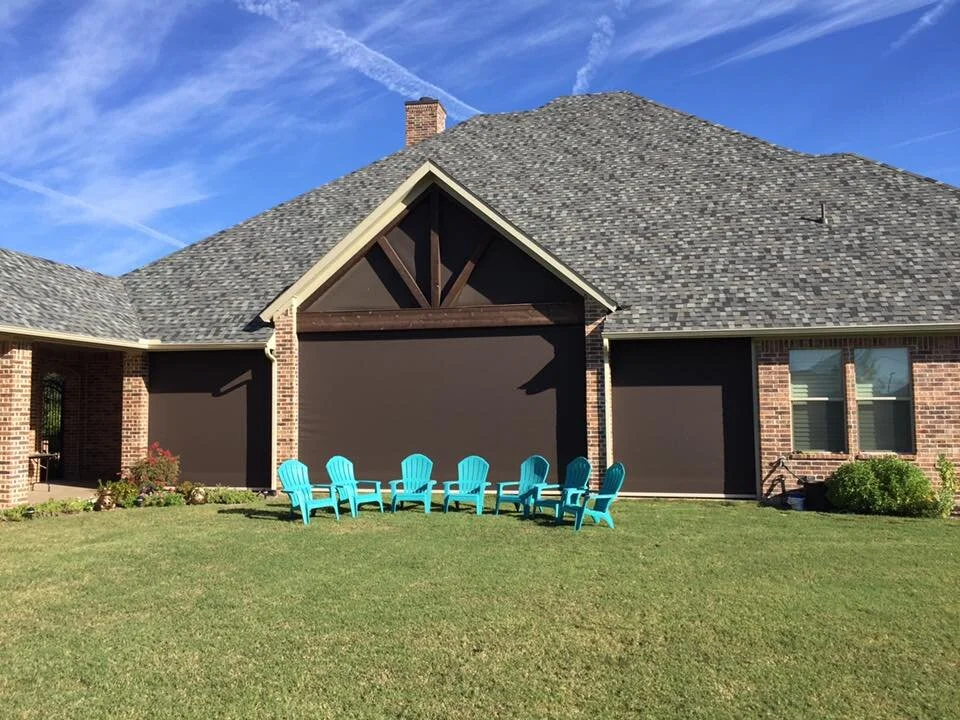 Backyard of a brick house with a large roof, a chimney, and screened-in porch. There are 8 turquoise Adirondack chairs arranged on the lawn in front of the screens.
