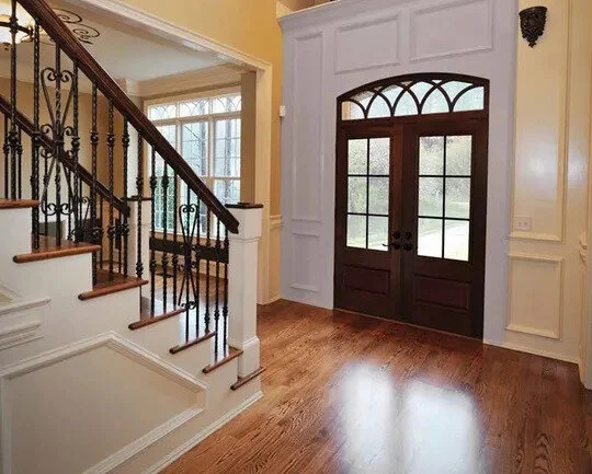 Entryway with wooden front door, glass panels, & staircase with decorative iron railing.