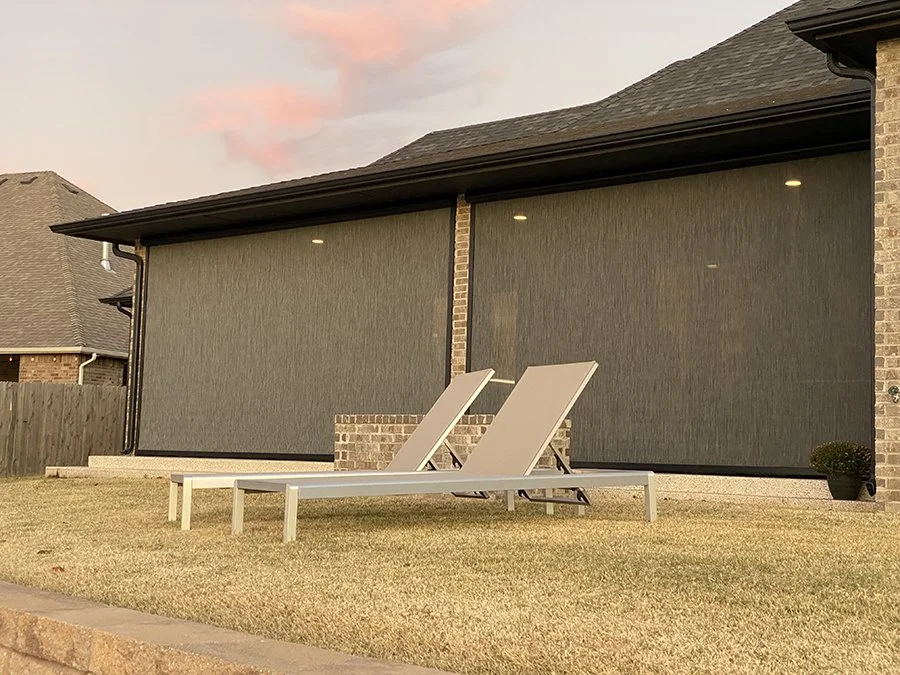 Backyard with two lounge chairs on a white wooden table, located on a well-kept grassy lawn, with a house in the background featuring a fly screen and brick walls, under a partly cloudy sky at sunset.