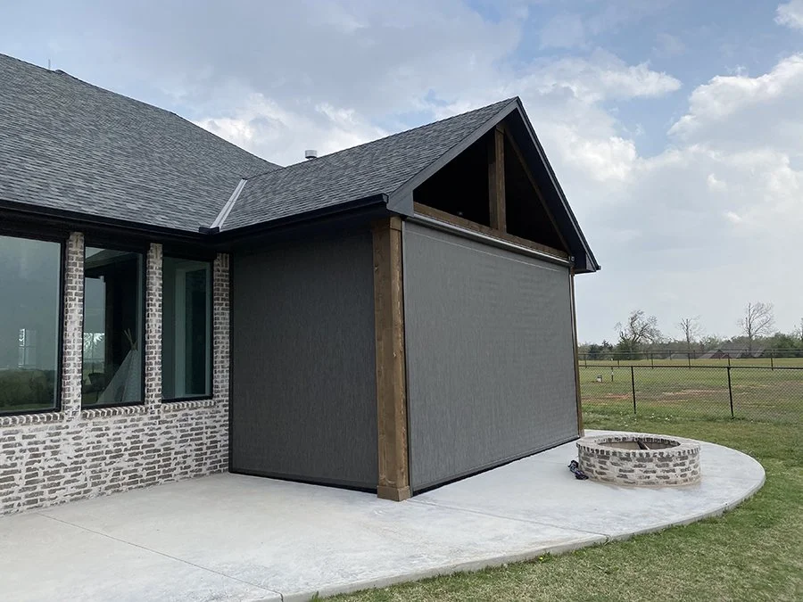Exterior of a house under construction with a screened-in porch, brick wall, and a small stone fire pit on a concrete patio.