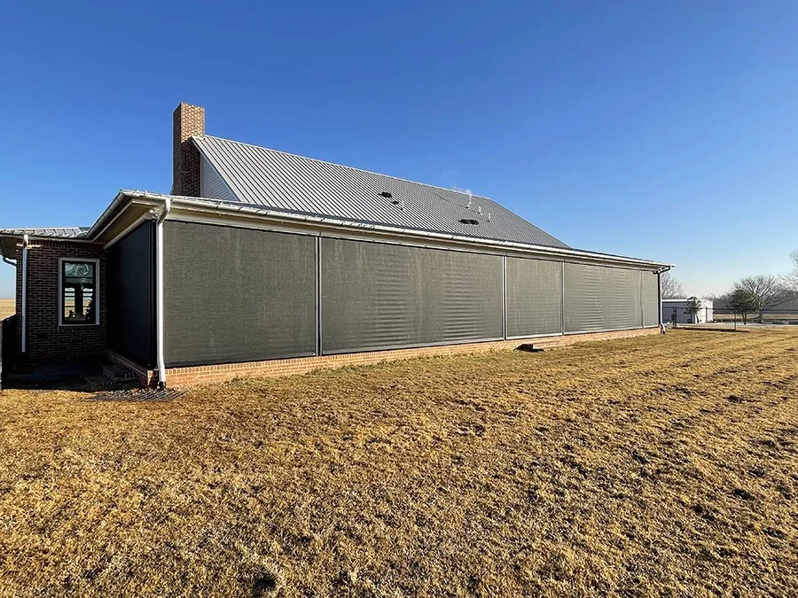 A large house with a metal roof and brick interior wall, with screened porch walls, on a grassy yard under a clear blue sky.
