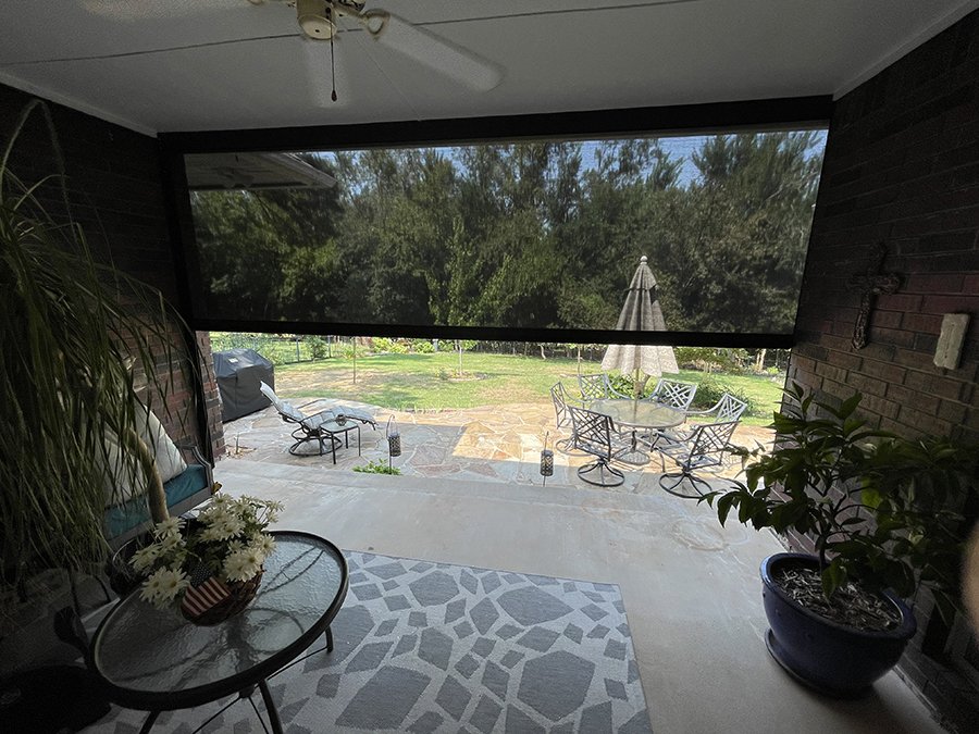 View of a backyard patio with outdoor furniture and a large window screen overlooking trees and grass.