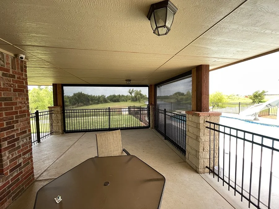 Covered patio with a table and chairs, overlooking a fence, yard, pool, and water slide in the background.