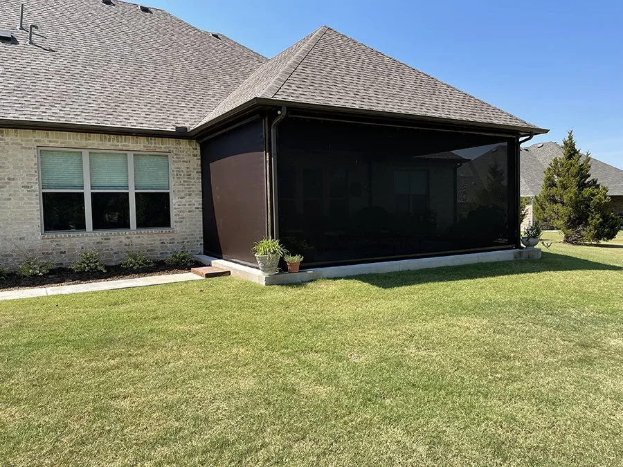 Backyard with a screened porch attached to a brick house, green lawn, and some potted plants.