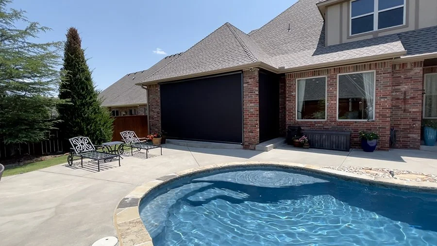 Backyard with a swimming pool, two metal patio chairs, potted plants, and a brick house with large windows.