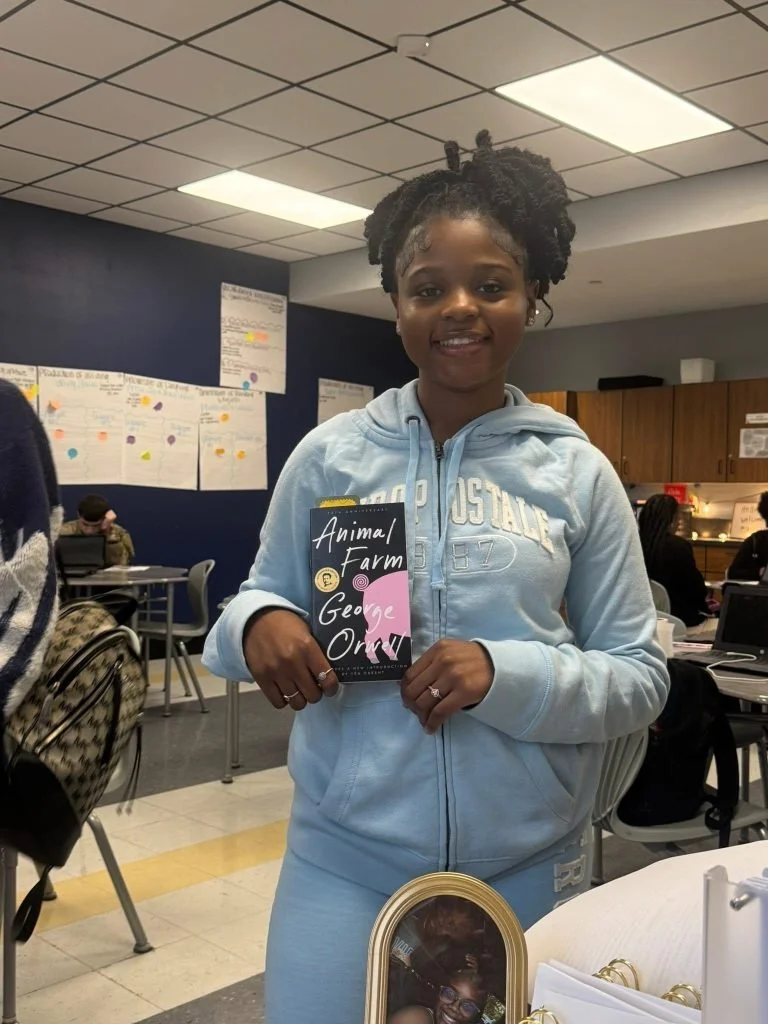 A young girl holds a copy of the book Animal Farm by George Orwell. CFM Vicki's Books for Kids Fund
