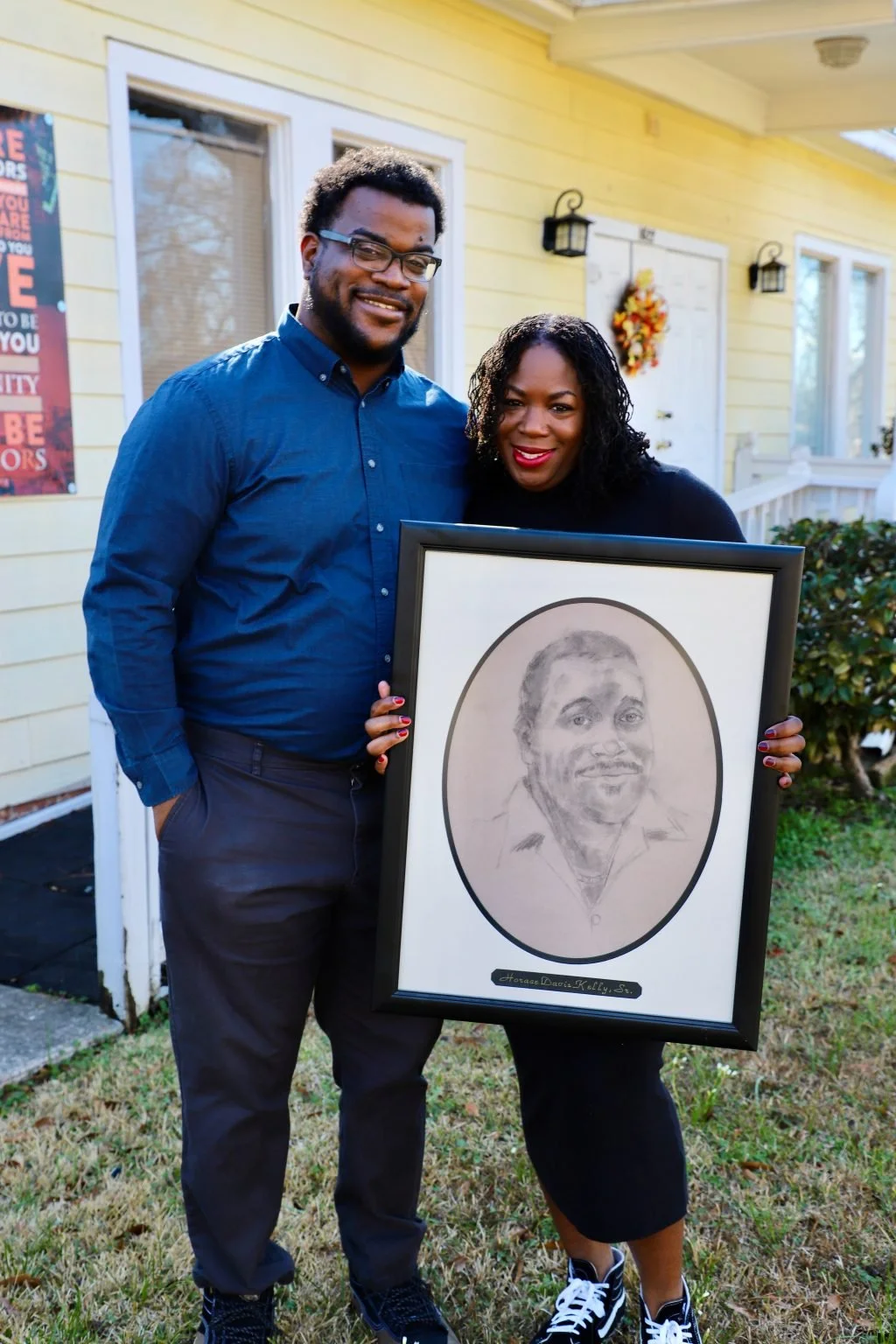 Ashlee and Akili Kelly hold up a drawing of Horace Kelly outside the “yellow house,” home to the Mid-City Community Development Corporation.
