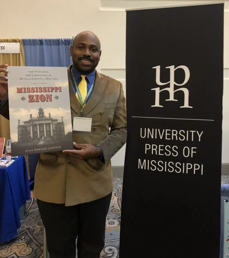 Evan Howard Ashford stands with his book, Mississippi Zion, next to a University Press of Mississippi sign.
