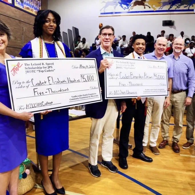 a group of people, including a young woman in a graduation gown, hold large checks.