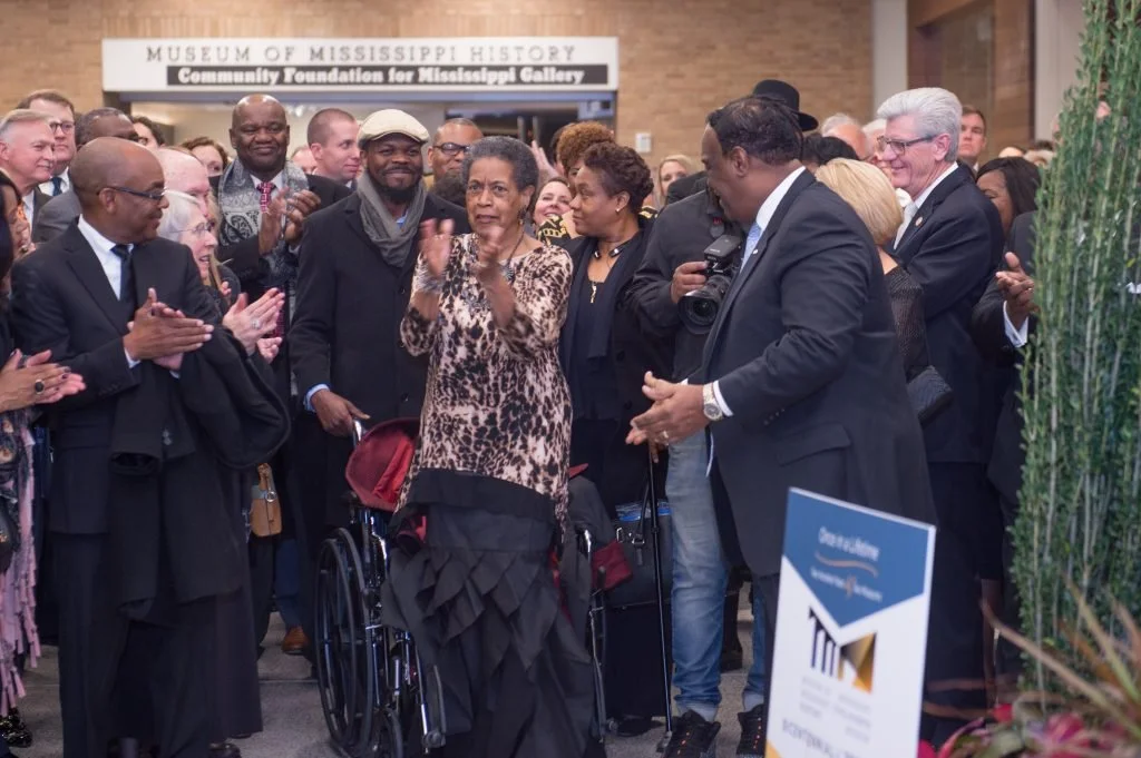 A crowd, including Myrlie Evers (center), claps during the opening of the Two Mississippi Museums. The Community Foundation for Mississippi Gallery at the Museum of Mississippi History can be seen in the background.