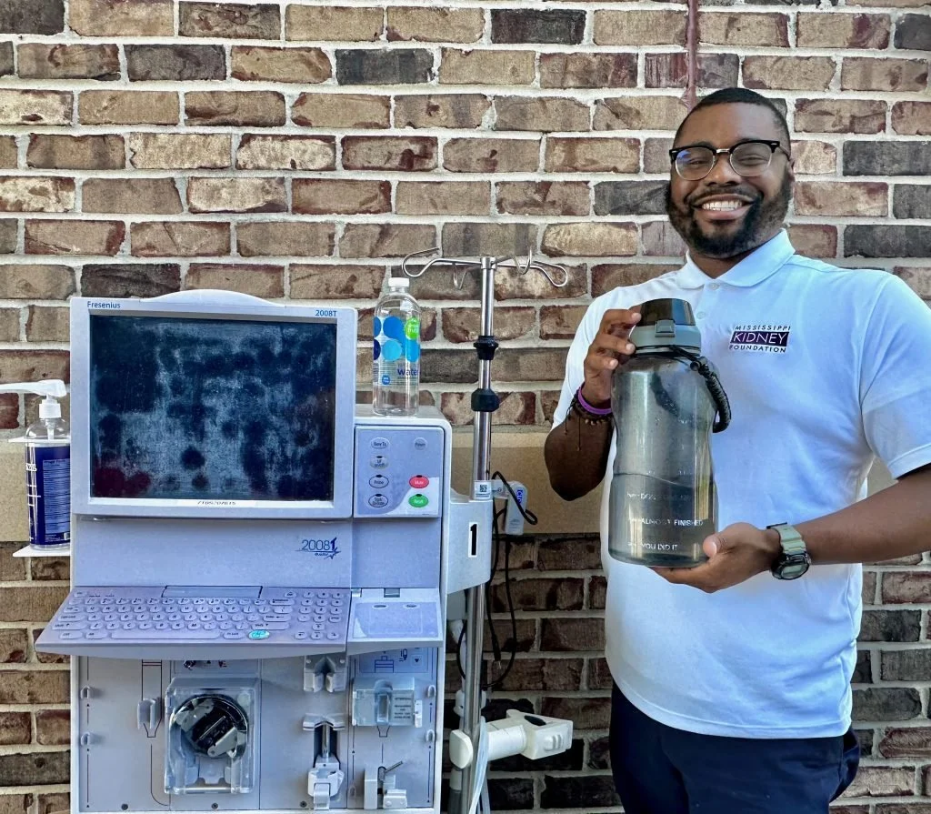 Mississippi Kidney Foundation’s executive director, TJ Mayfield, stands with a dialysis machine that will be able to use bottled water provided by the grant.