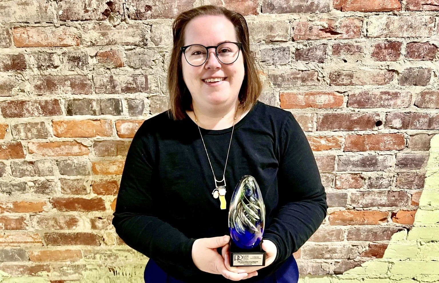 Sophie McNeil Wolf, APR, Community Foundation for Mississippi, stands with an award in front of a brick wall.