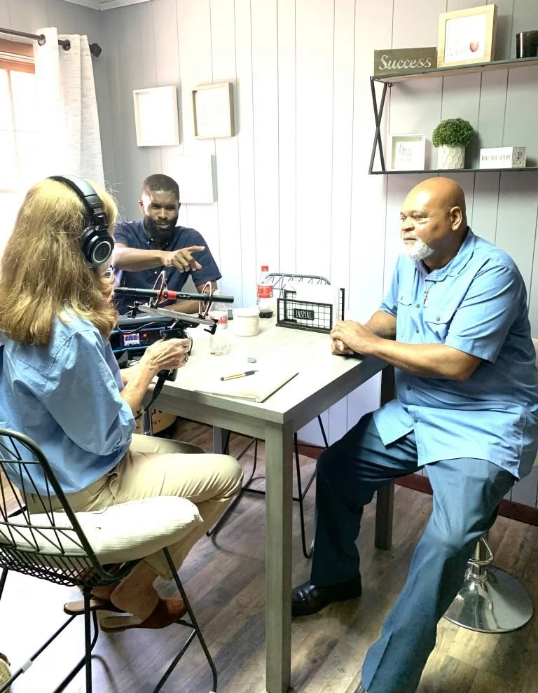 Two men and one woman site around a table recording an interview