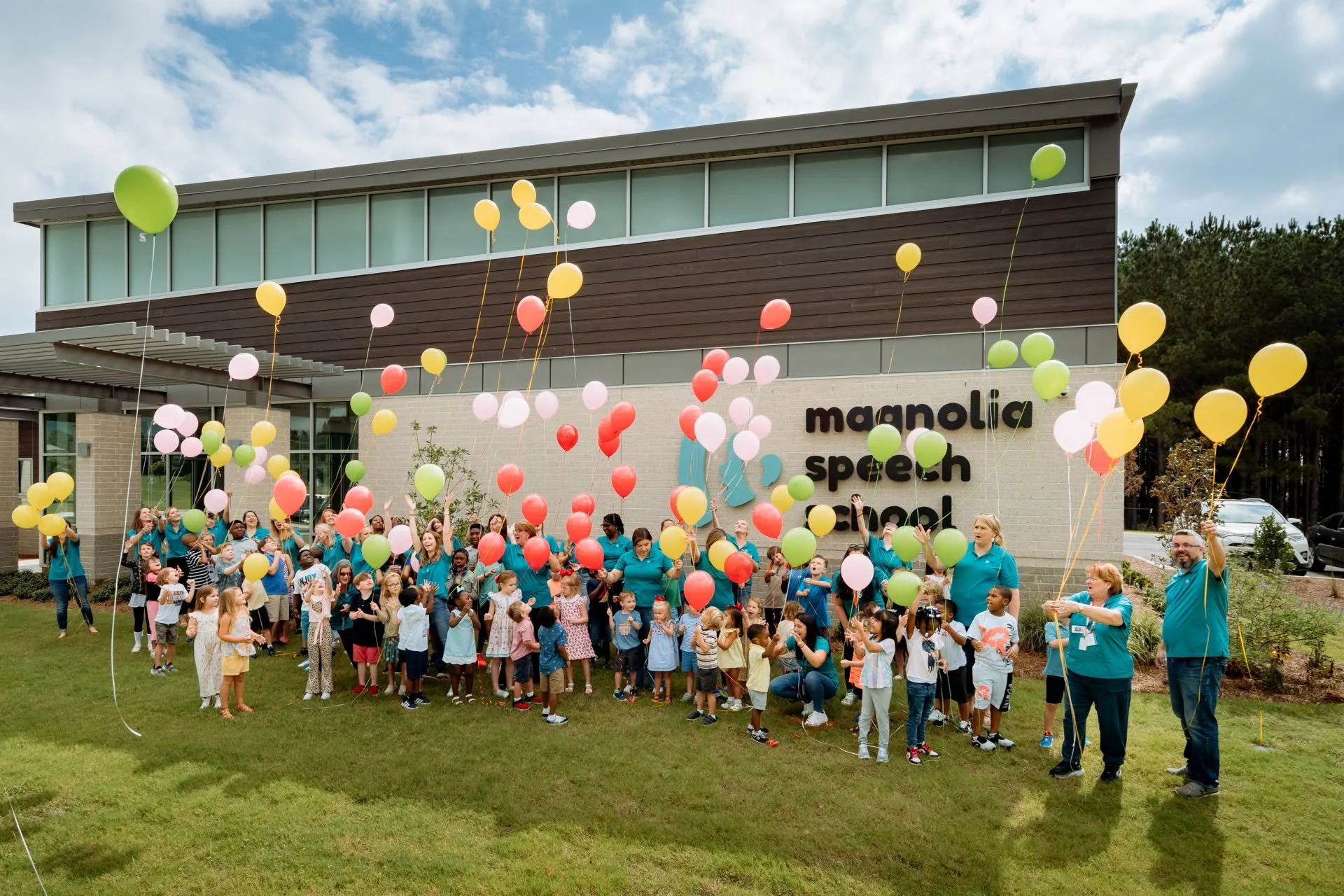 Magnolia Speech School children and staff celebrating outside it's school building with colorful balloons.