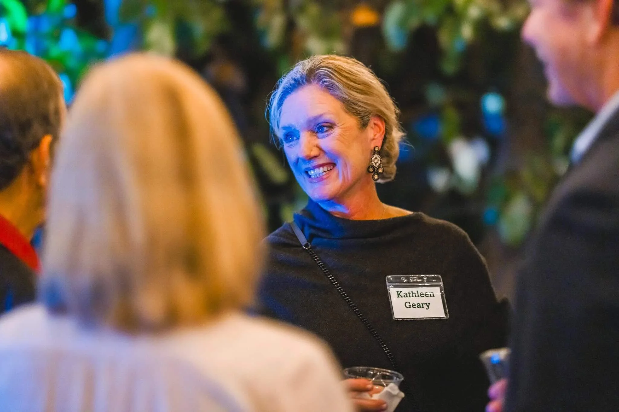 A woman at CFM's Friendsgiving event. The background is decorated with colorful lights and greenery.