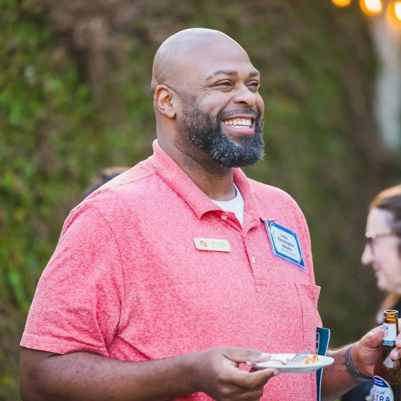 A smiling man with a beard in a pink shirt holding a plate of food at CFM's Giving Forward event.