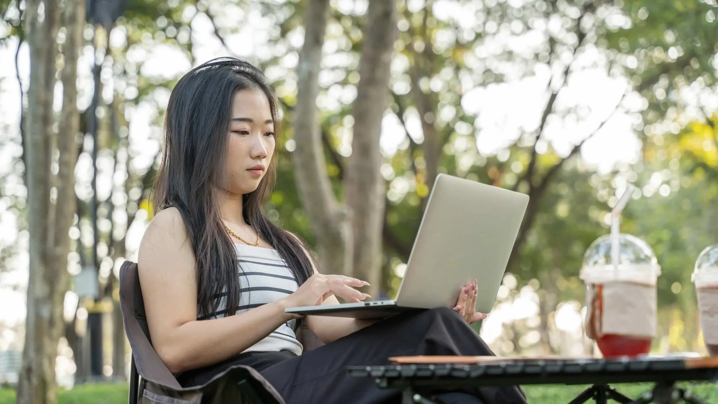 Young Asian woman works on a computer while sitting outside