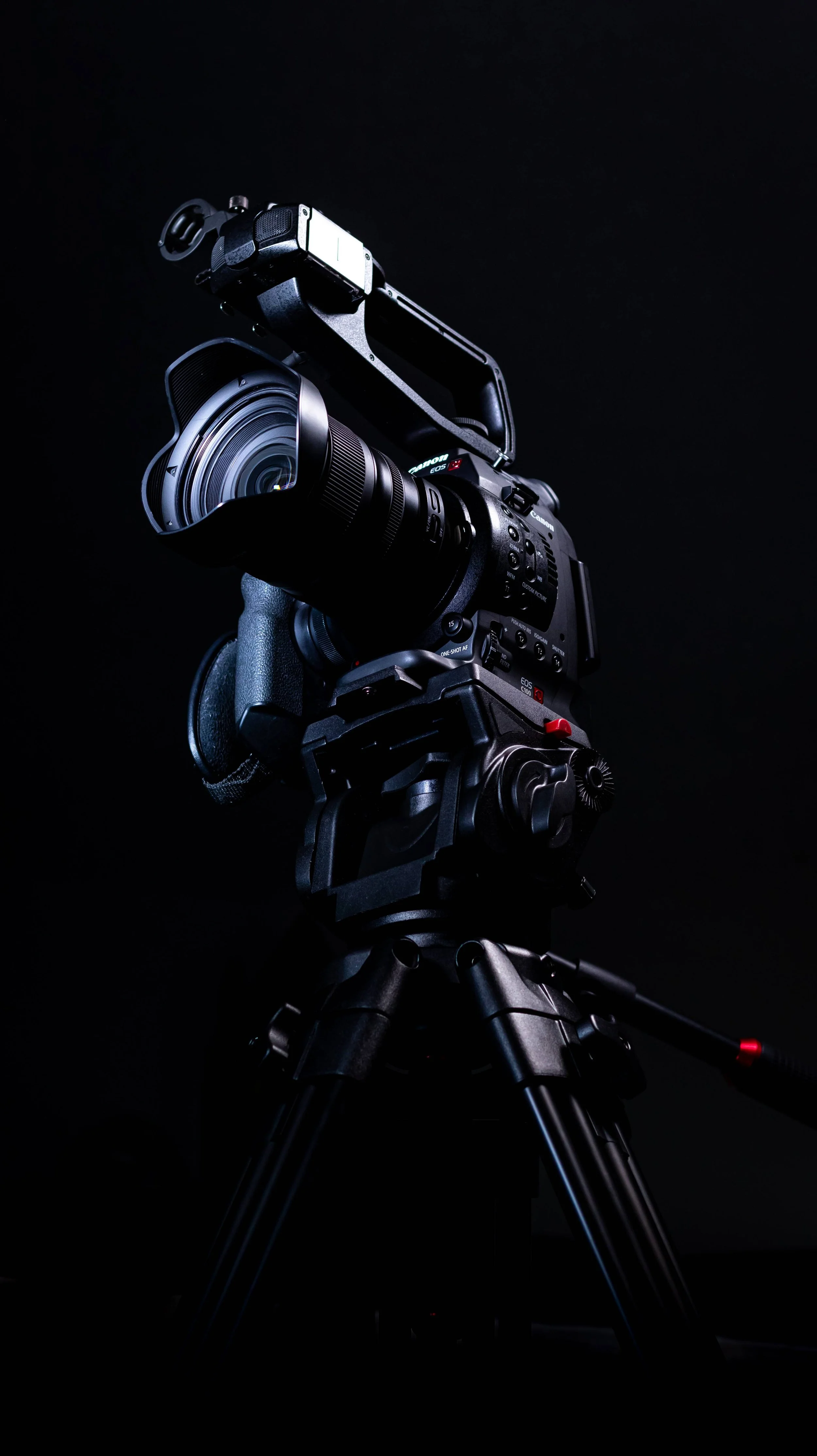 A professional video camera mounted on a tripod against a dark background.