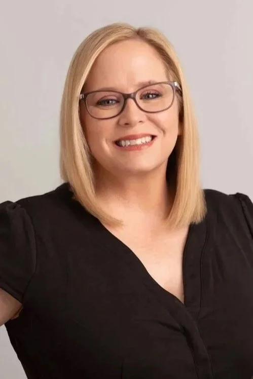 A woman with blonde hair, glasses, and a black top smiling at the camera.
