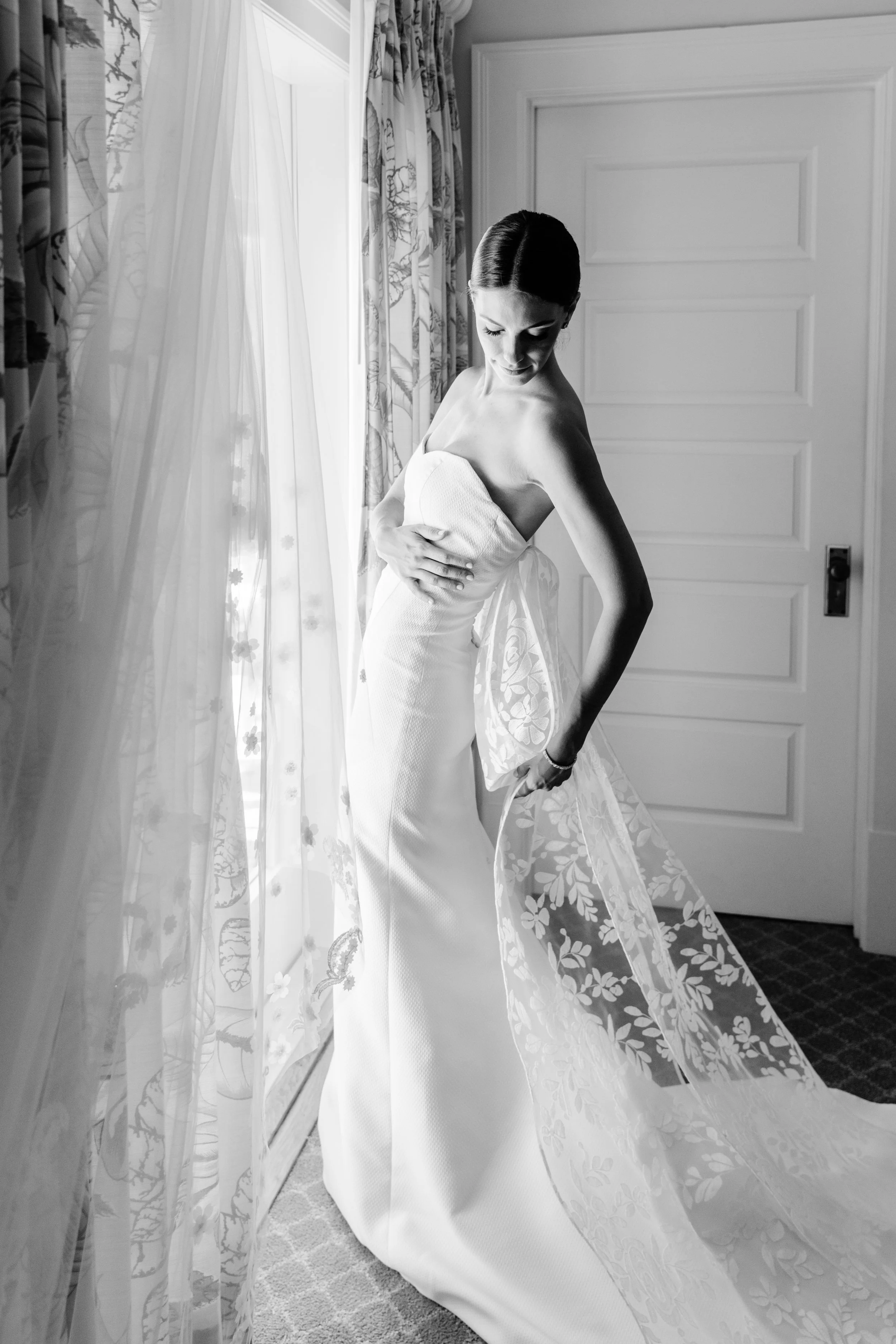 Black and white image of bride adjusting her dress at window in Gasparilla Inn
