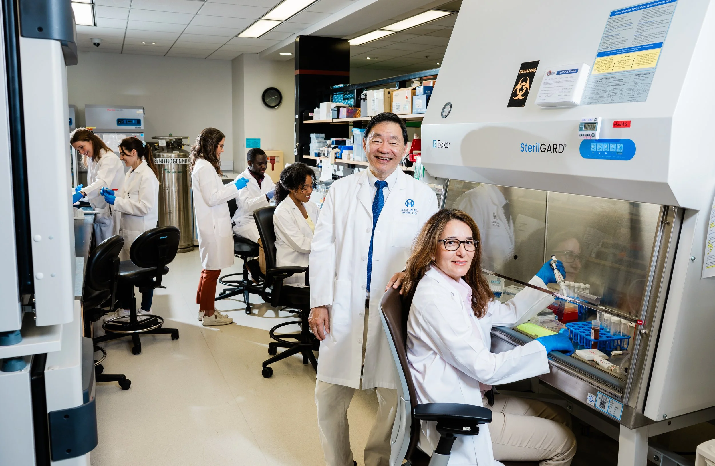 Group of diverse scientists working in a laboratory, with one woman using a biological safety cabinet, and others performing experiments at the lab benches.