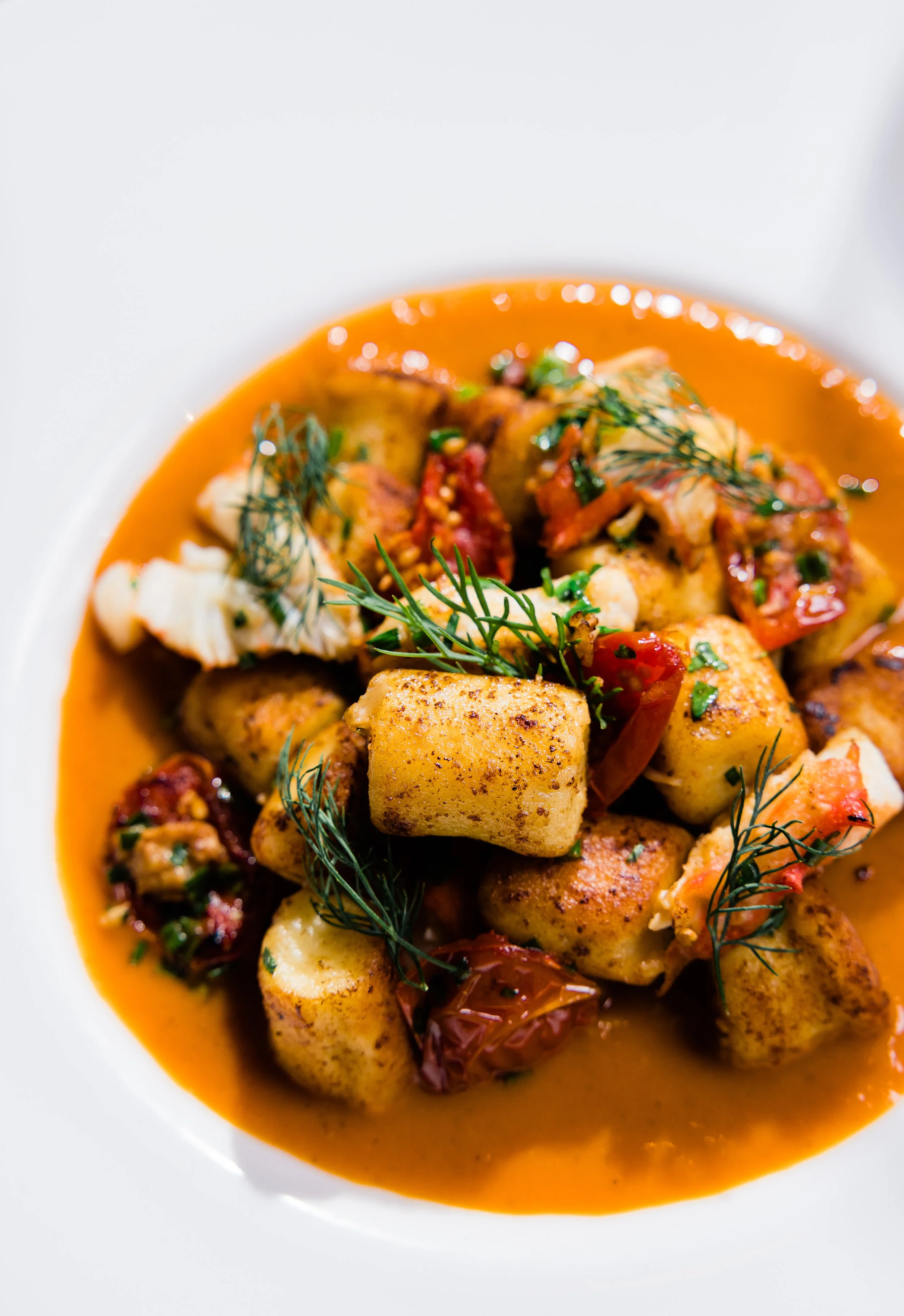 A bowl of seafood stew with chunks of fish, potatoes, and herbs in a tomato-based broth.