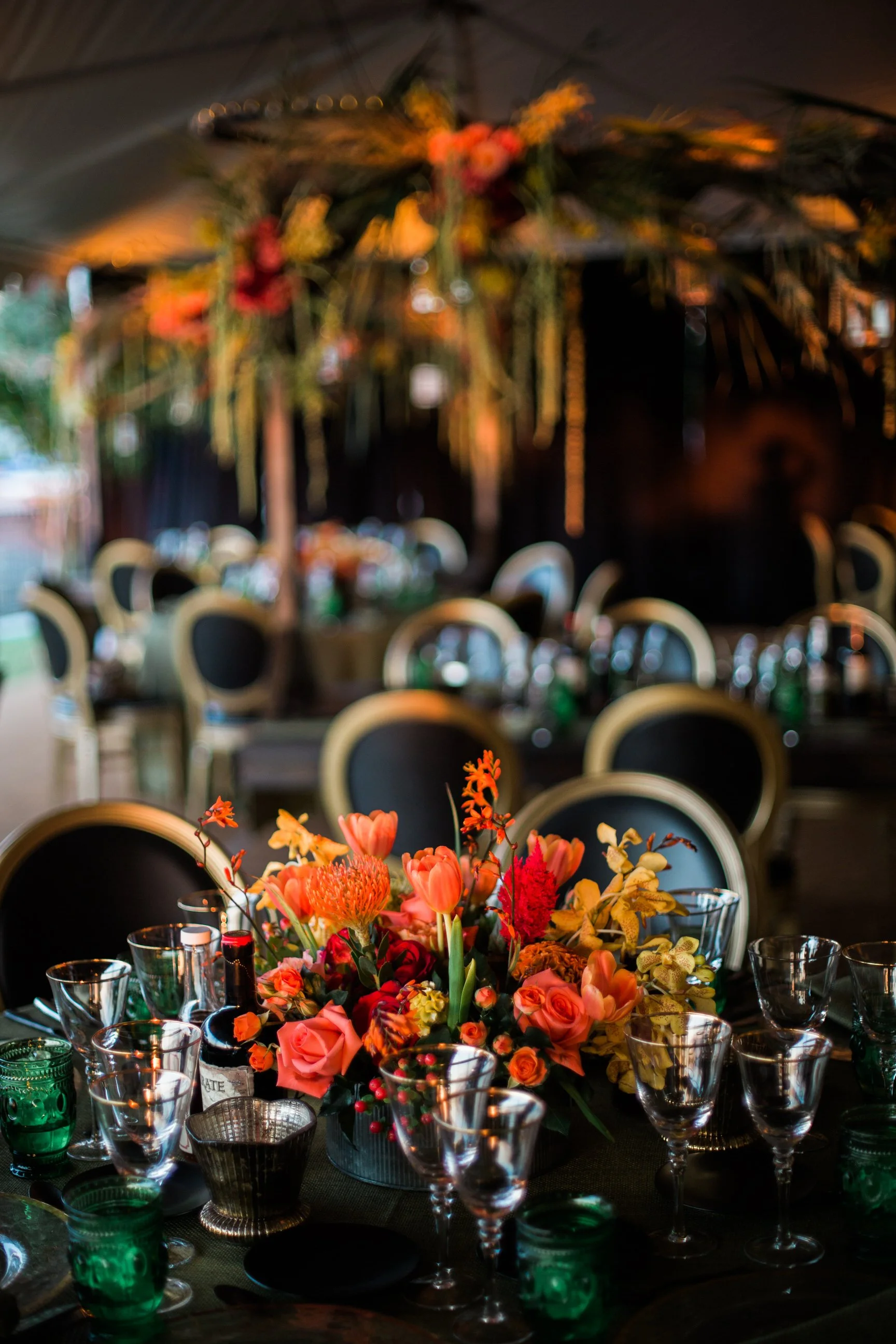 A colorful floral centerpiece surrounded by clear glassware on a dining table at an event or celebration.