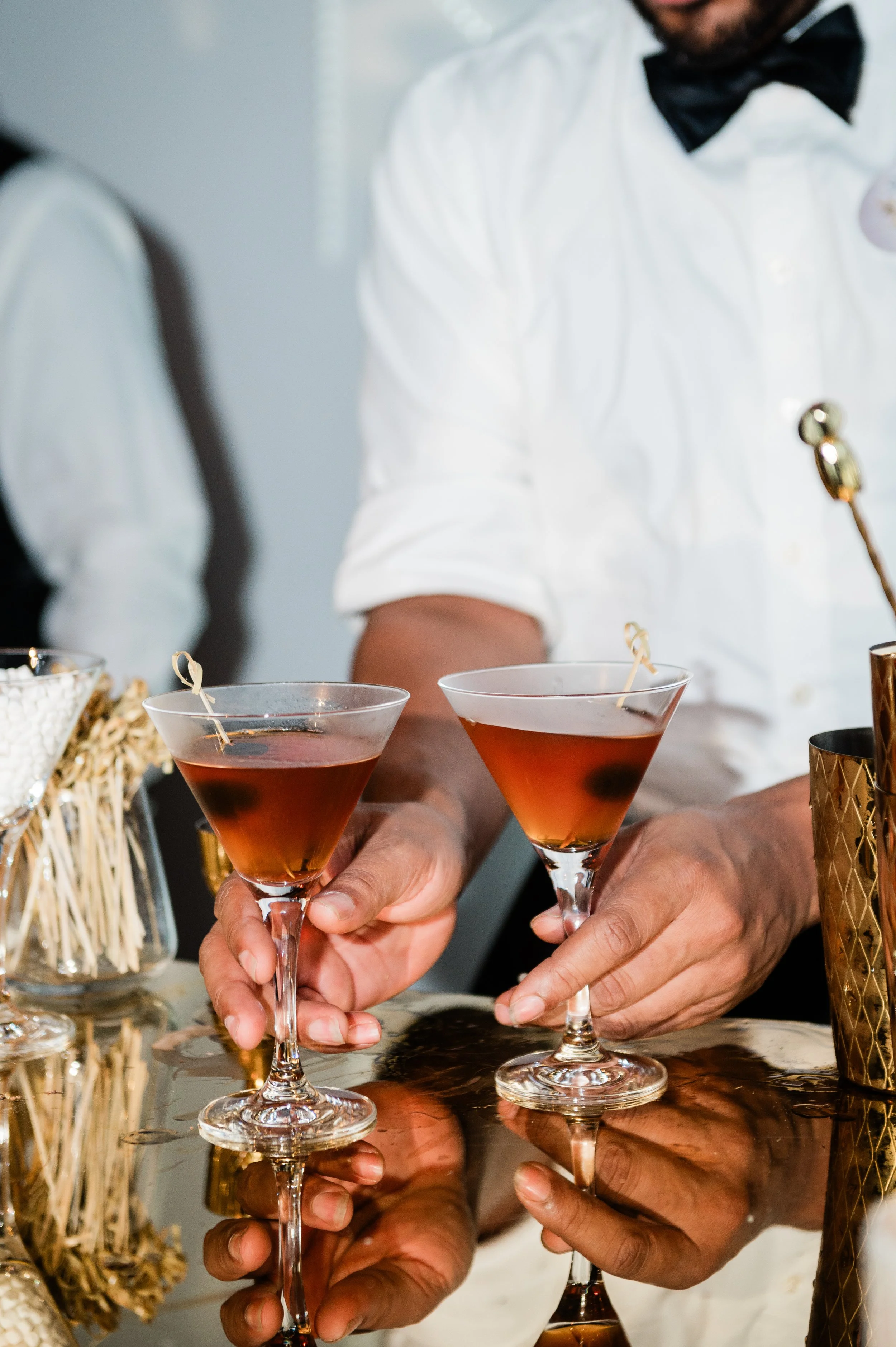 Two people dressed in tuxedos and white shirts holding cocktail glasses with red drinks, preparing to toast.