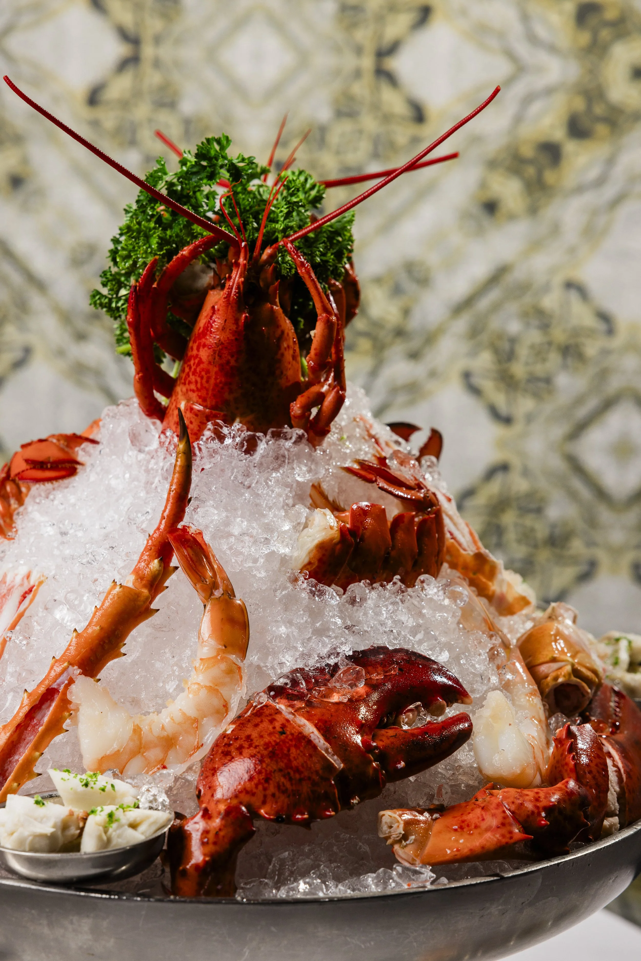 Lobster, shrimp, and seafood on crushed ice with parsley and cocktail sauce served on a metal tray.