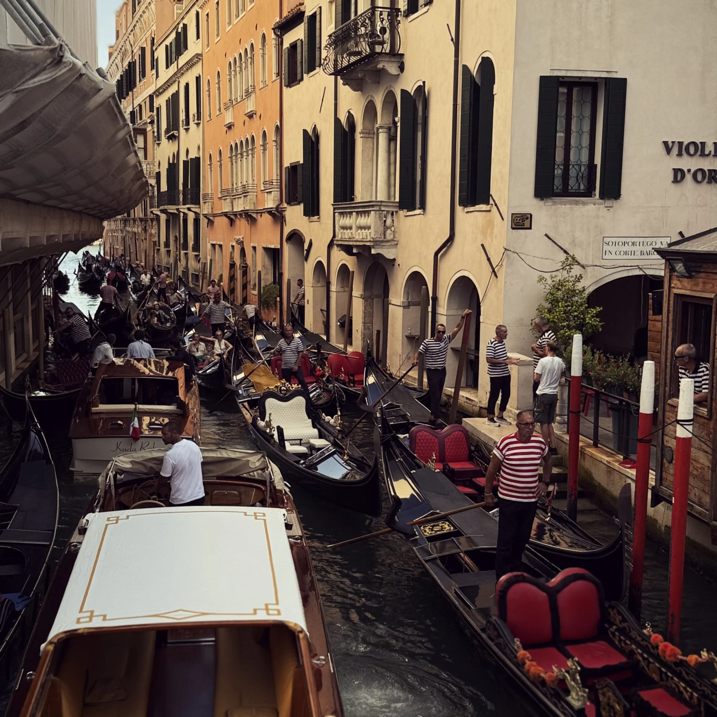 black gondolas with red seats, gondoliers in striped shirts, wooden boat taxis with white top