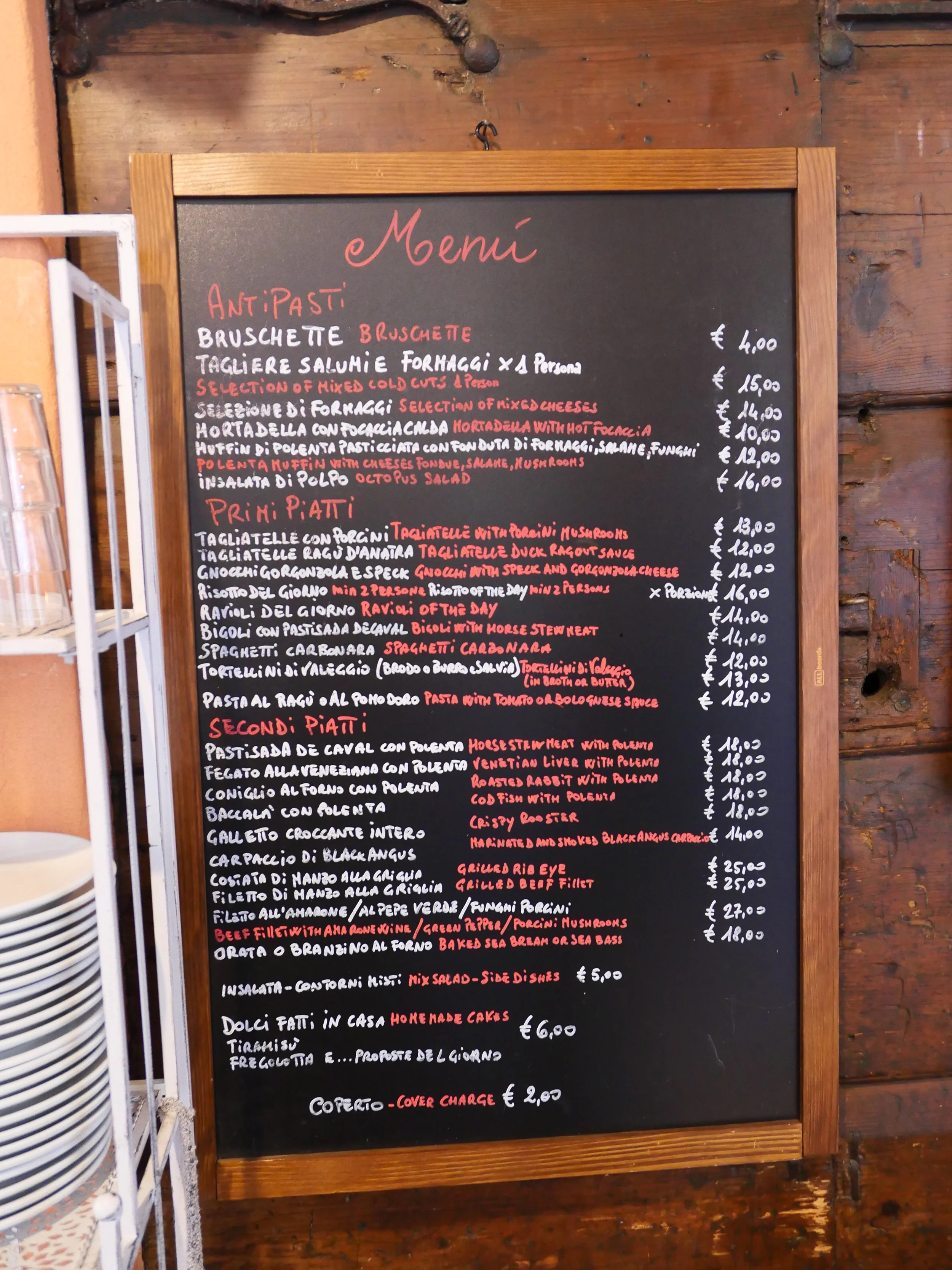 Black chalkboard with white Italian text and red English translation of menu items