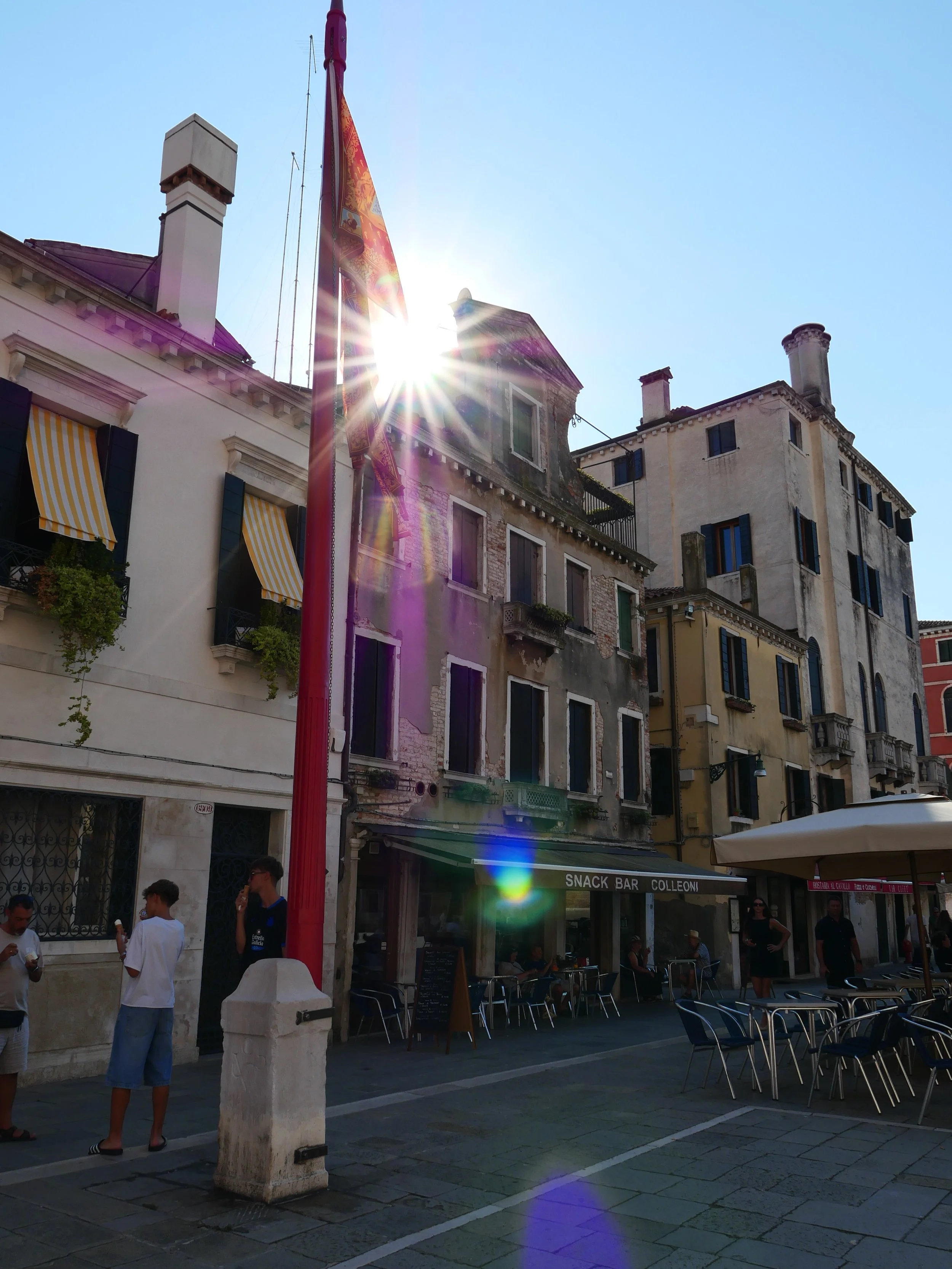 sun flare in street scene of Venice Italy with cafe chairs and kids eating ice cream