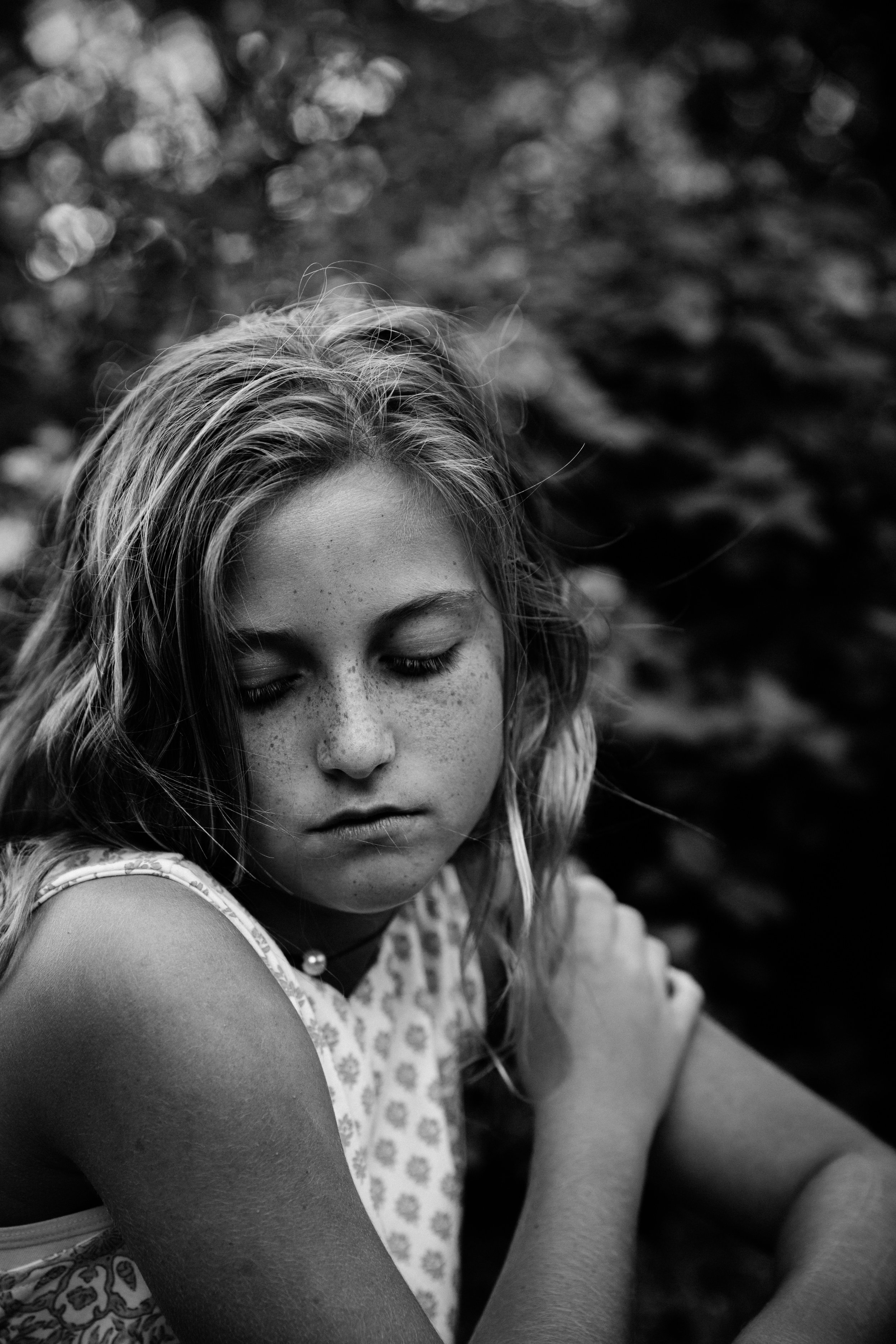 Black and white image of a young girl looking down with a pensive look on her face.