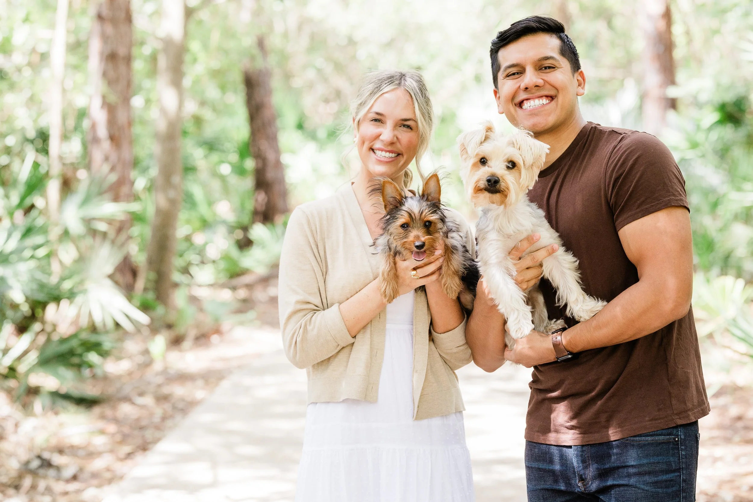 Smiling woman and man holding dogs in a forest setting.