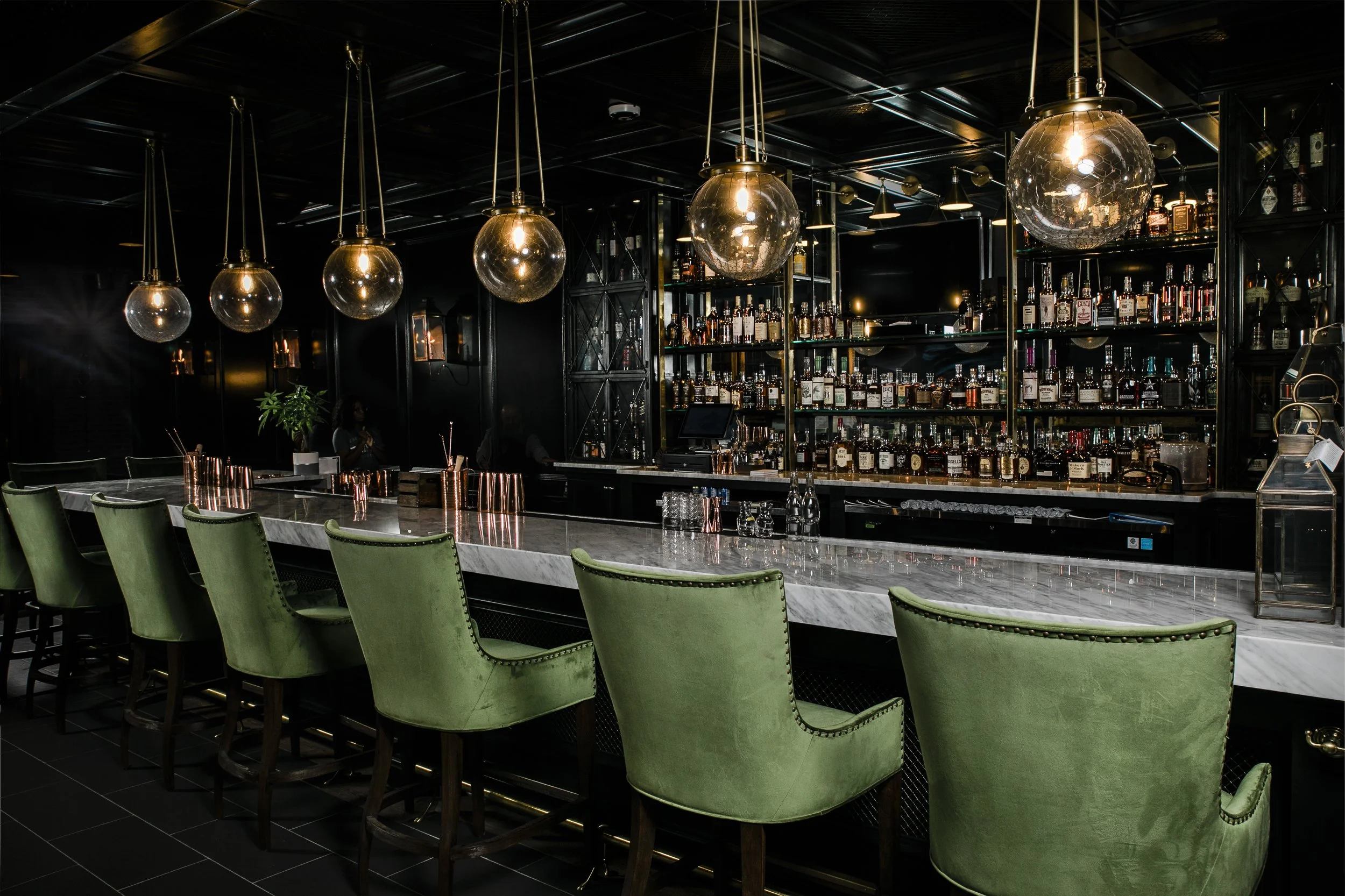 green chairs and glass globe pendants at bar for Urban Stillhouse