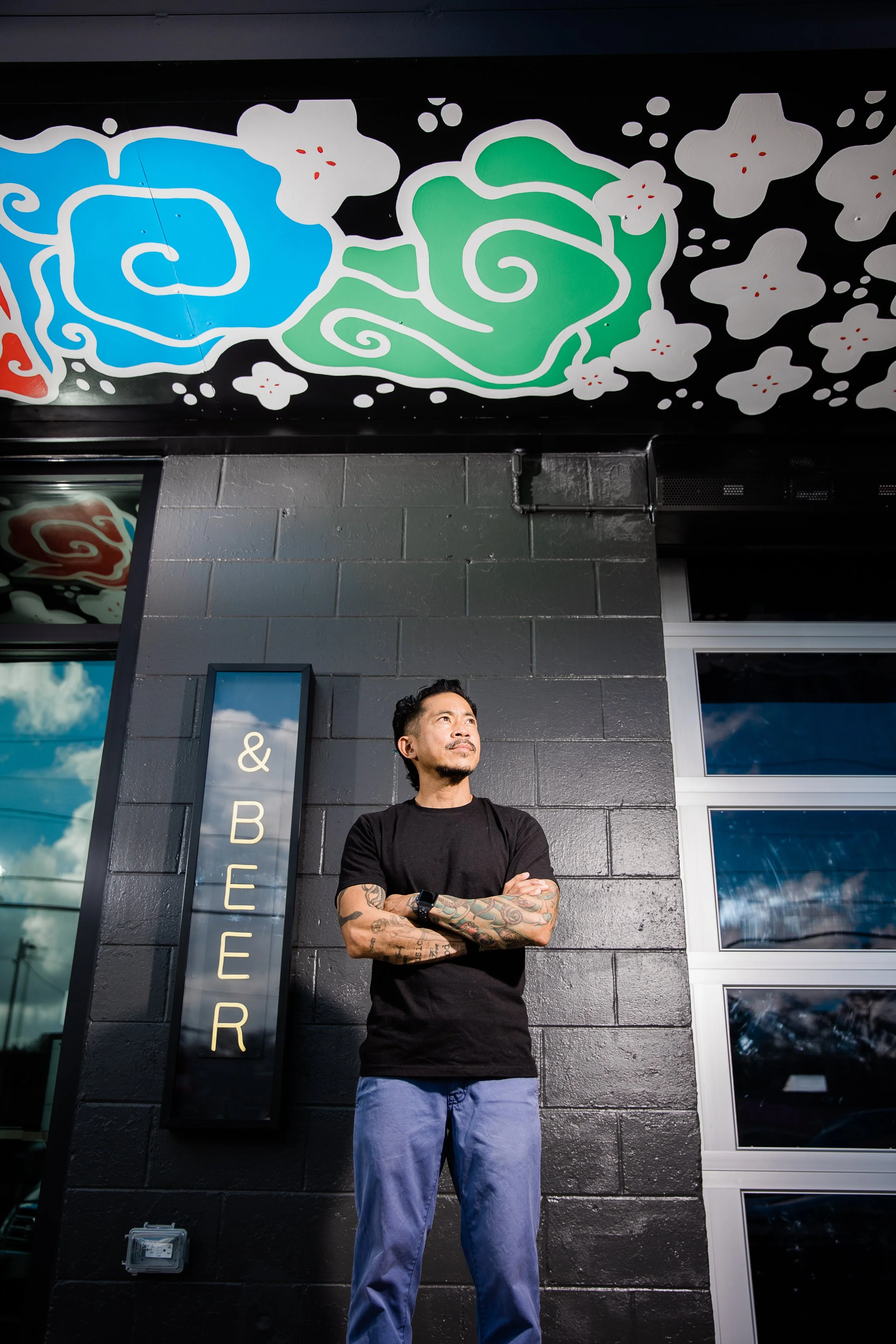 owner/chef of Gangchu poses with arms crossed in front of restaurant with mural above