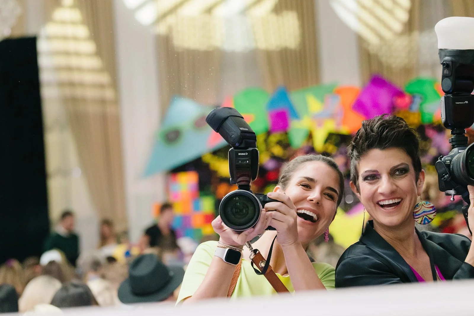 Marissa and Amy laugh with their cameras while photographing a bright 80s themed fundraiser for the Heart Gallery of Tampa