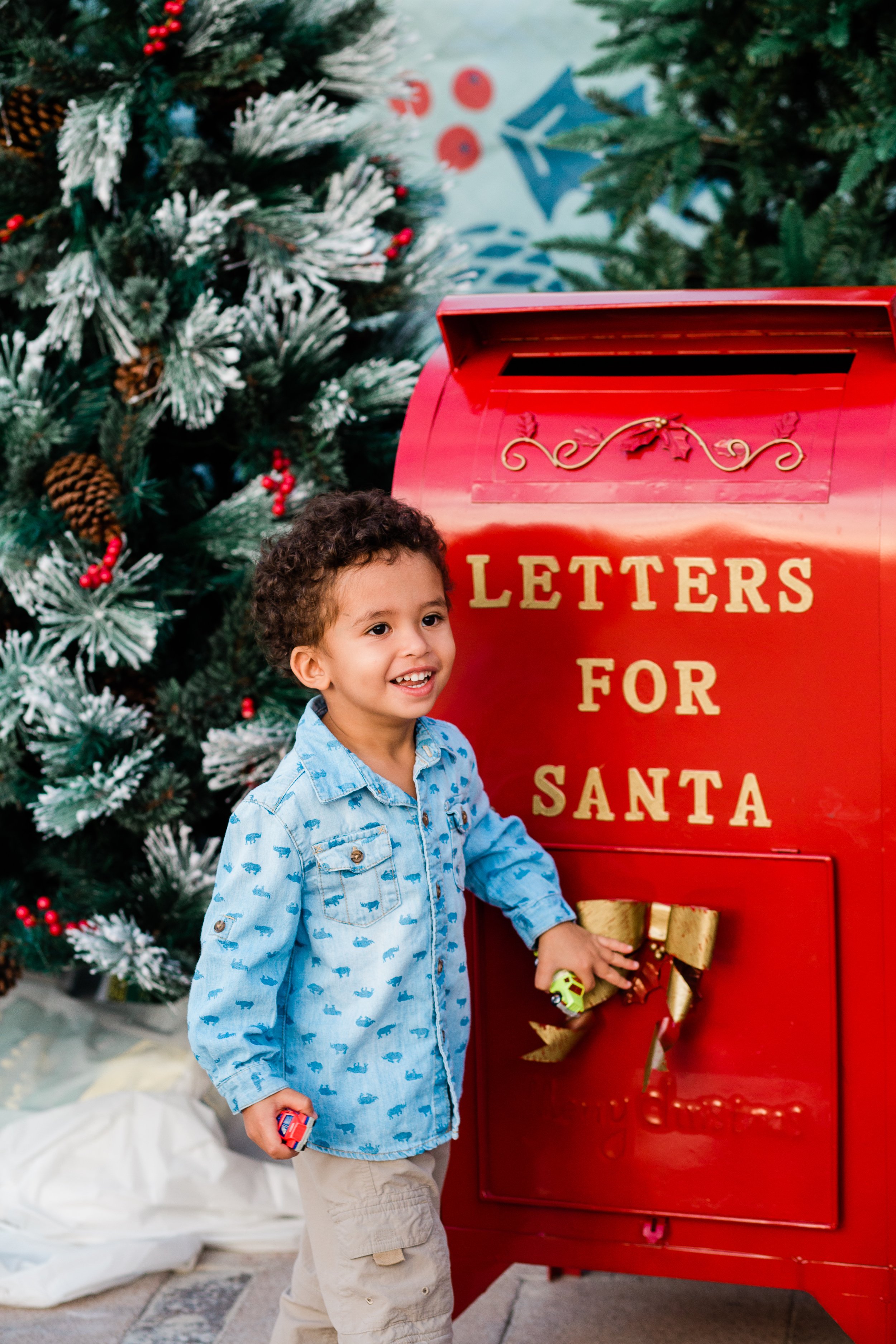 small boy in a blue shirt in front of a red Letters for Santa mailbox
