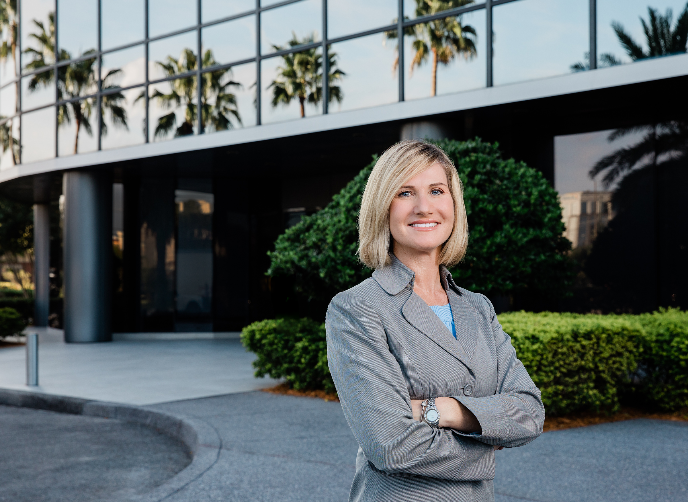 Executive woman stands outside Cogent Bank location. Palms are reflected in the glass building for Florida location context.
