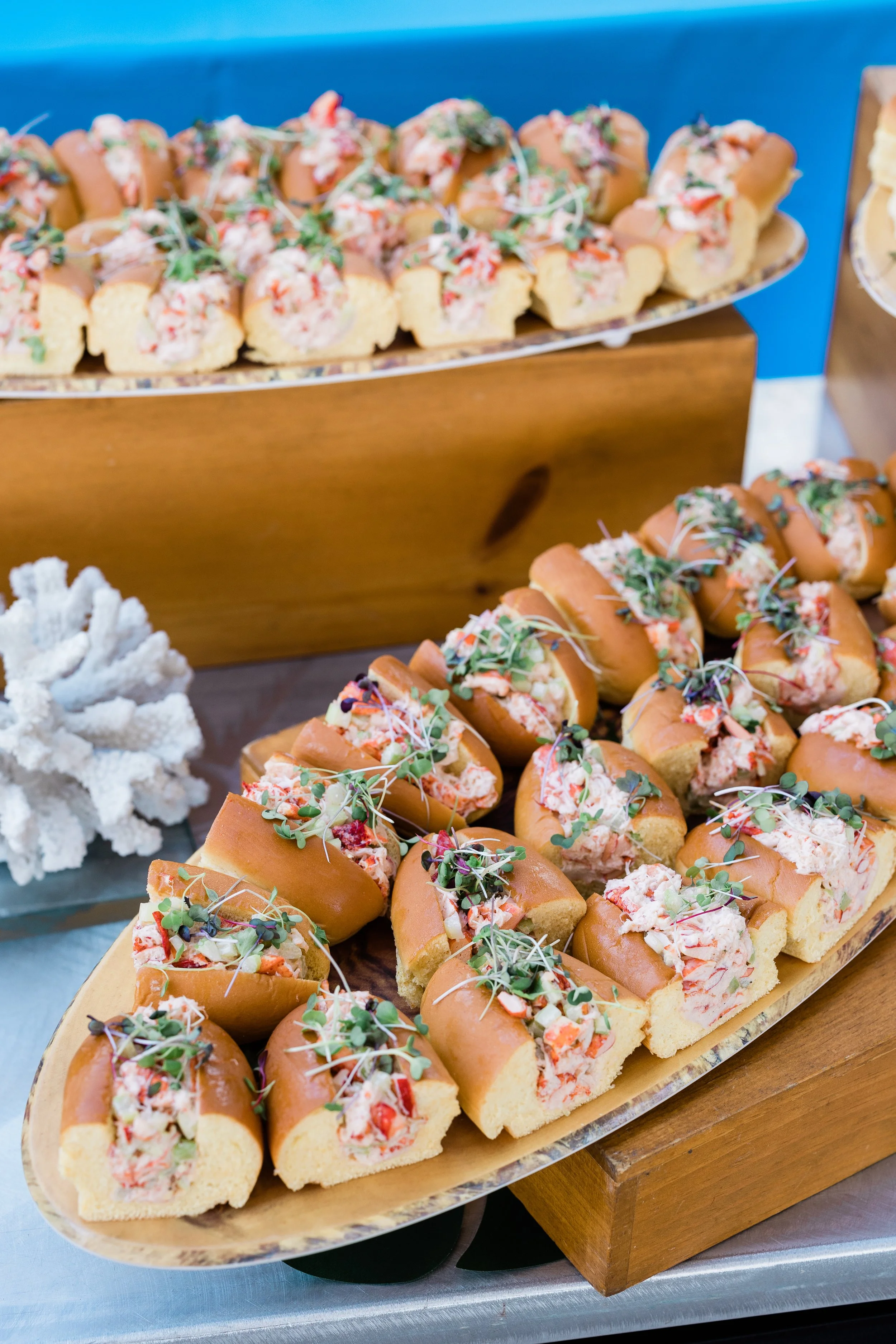Tray of small sandwiches with chopped vegetables and microgreens, served on a wooden platter at a buffet.