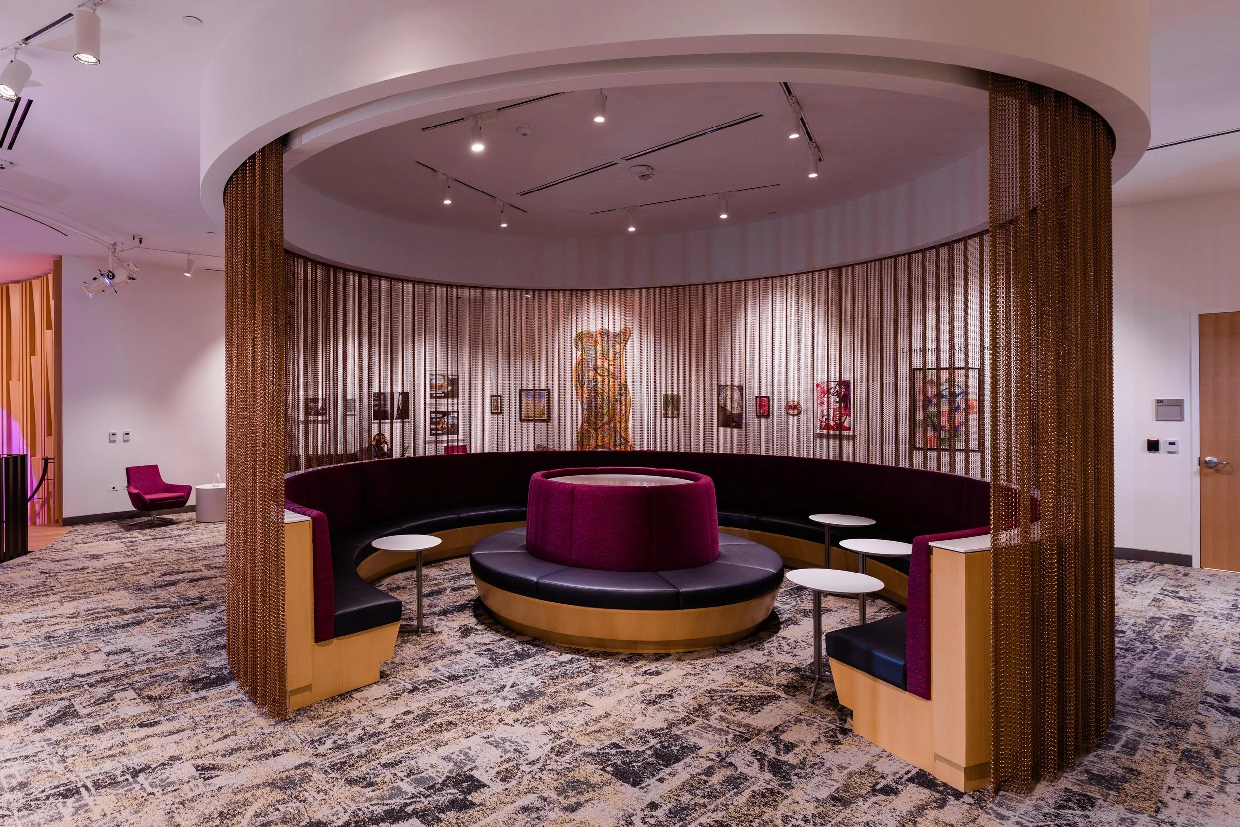 Interior of a modern lounge or waiting area with curved purple and black seating, small white tables, artistic artwork including a colorful tiger sculpture, and decorative brown metal curtains dividing the space.